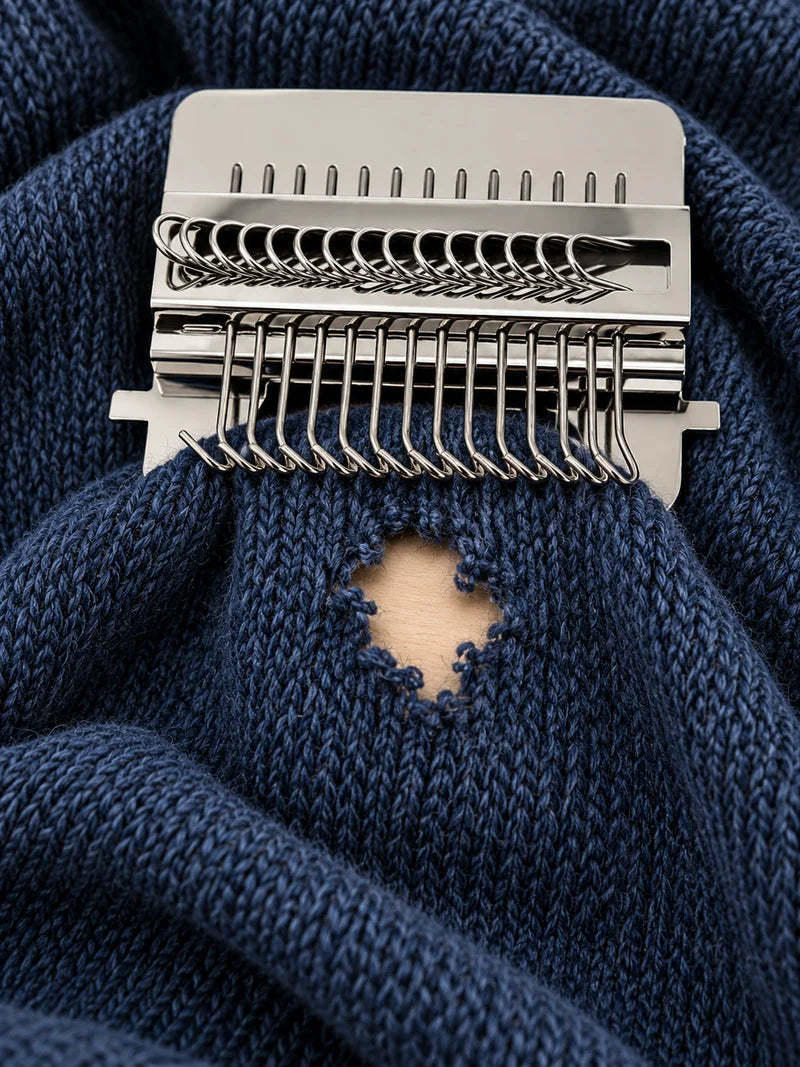 Métier à repriser installé au-dessus d’un trou dans une maille bleu marine.